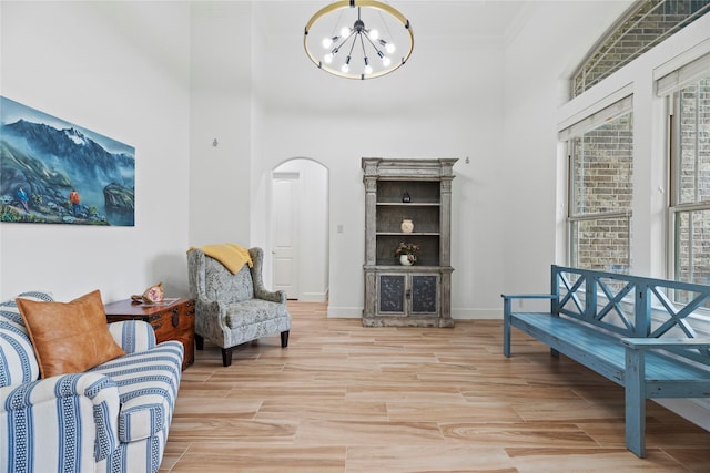 sitting room with baseboards, ornamental molding, wood finished floors, arched walkways, and a notable chandelier