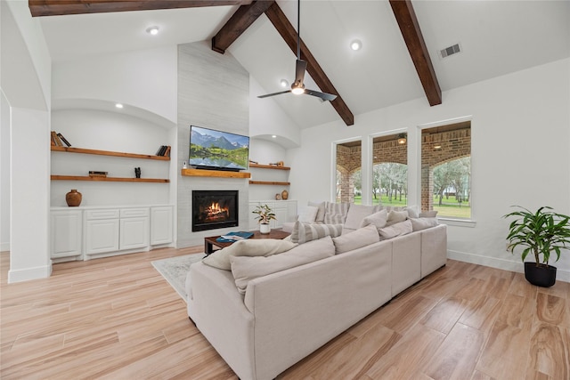 living room featuring beamed ceiling, high vaulted ceiling, a large fireplace, light wood finished floors, and baseboards