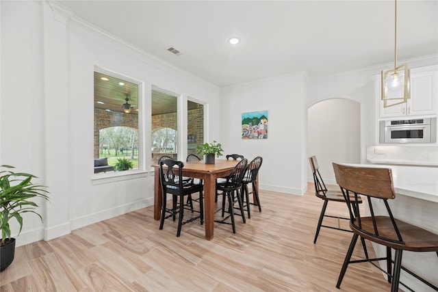 dining room with visible vents, crown molding, baseboards, light wood-type flooring, and arched walkways