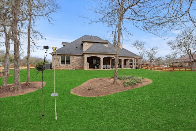 rear view of house featuring a lawn, fence, cooling unit, a shingled roof, and brick siding