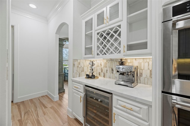 bar featuring tasteful backsplash, crown molding, beverage cooler, arched walkways, and a bar