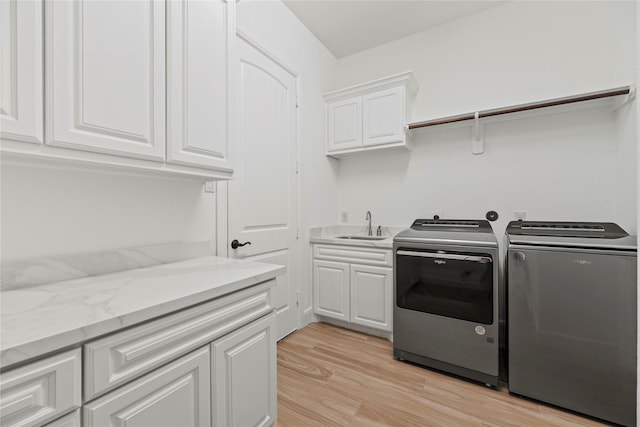 clothes washing area featuring washer and dryer, cabinet space, light wood finished floors, and a sink