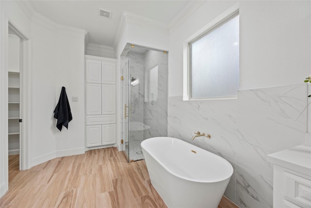 bathroom featuring visible vents, a marble finish shower, a soaking tub, crown molding, and tile walls