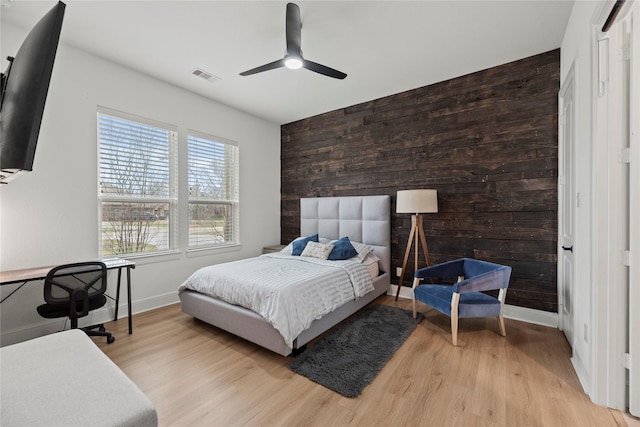 bedroom with visible vents, wooden walls, light wood finished floors, baseboards, and an accent wall