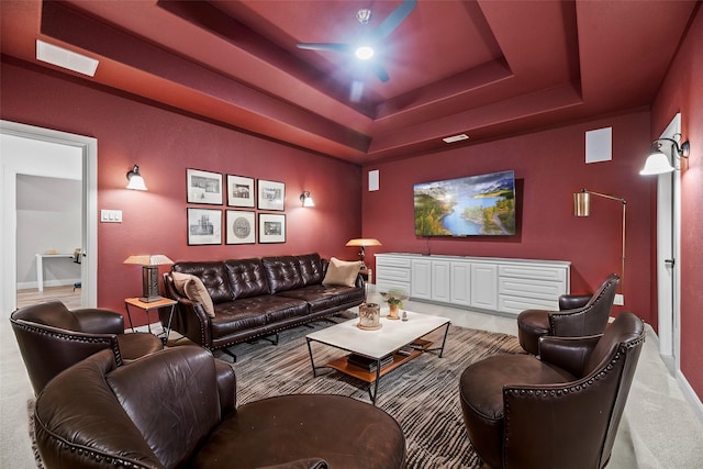 living area with a raised ceiling, light carpet, and a ceiling fan