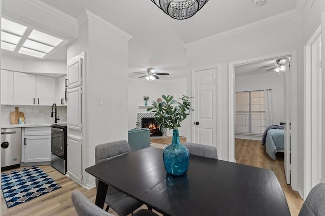 dining space with light wood finished floors, crown molding, and a lit fireplace