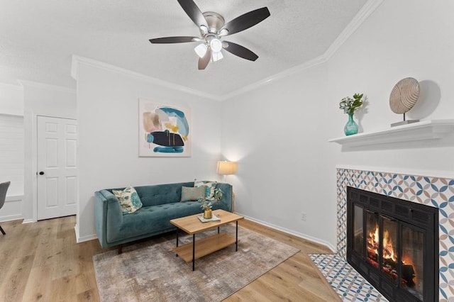 living area with ornamental molding, a ceiling fan, a tiled fireplace, wood finished floors, and baseboards