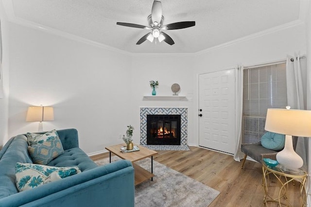 living room with baseboards, ceiling fan, ornamental molding, a tile fireplace, and wood finished floors