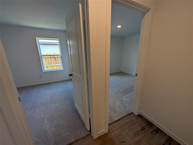 corridor with dark wood-style flooring, baseboards, and dark carpet