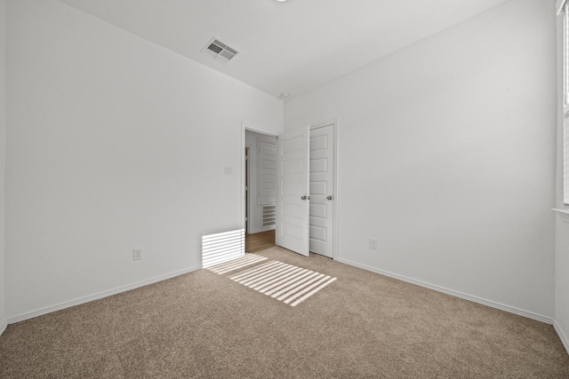 empty room featuring light carpet, visible vents, and baseboards