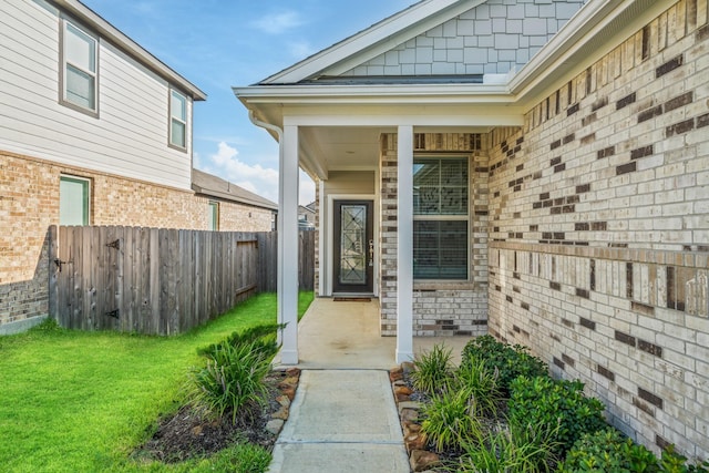 doorway to property featuring a yard, fence, and brick siding