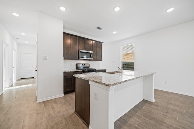 kitchen featuring visible vents, light wood finished floors, a sink, stainless steel appliances, and dark brown cabinets