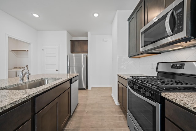 kitchen featuring independent washer and dryer, a sink, dark brown cabinetry, appliances with stainless steel finishes, and tasteful backsplash