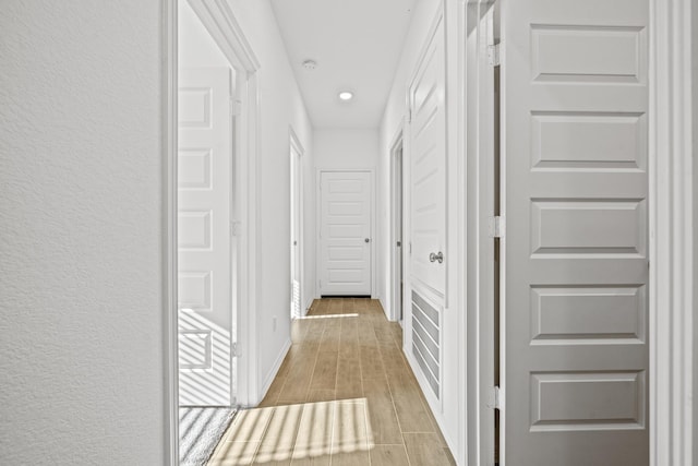 hall featuring recessed lighting, a textured wall, baseboards, and wood tiled floor