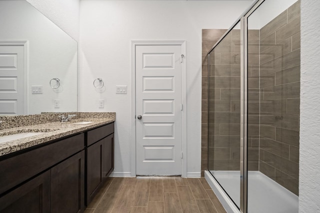 bathroom featuring double vanity, a shower stall, wood finish floors, and a sink