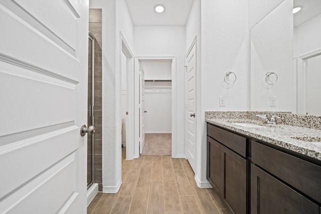 full bathroom featuring a sink, a shower stall, double vanity, a spacious closet, and wood tiled floor