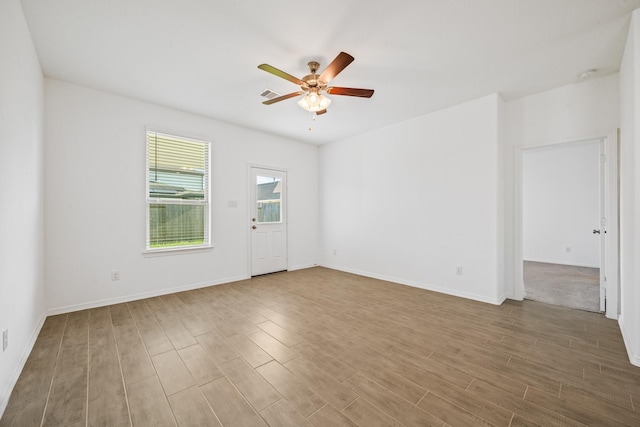 spare room with a ceiling fan, visible vents, wood finished floors, and baseboards