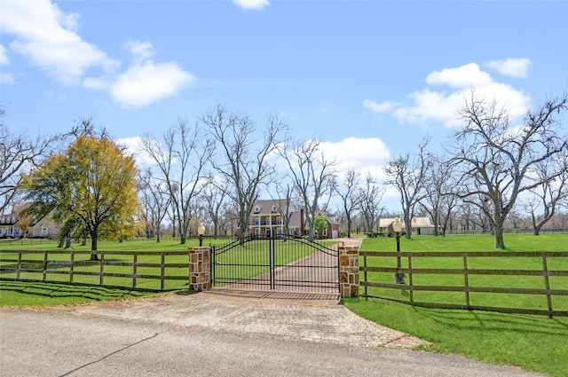 view of gate featuring a rural view, a lawn, and fence