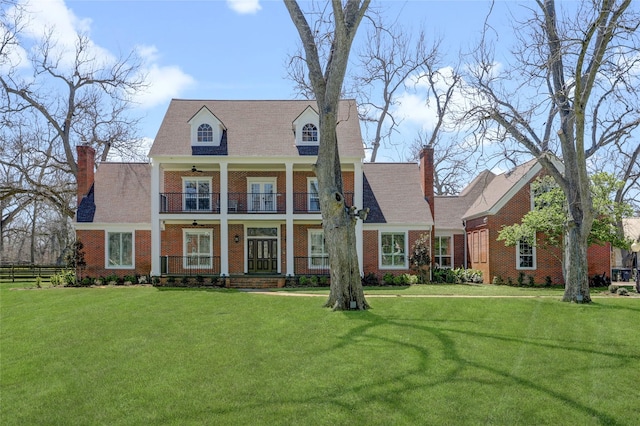 view of front of house with brick siding, a chimney, a front yard, and a balcony