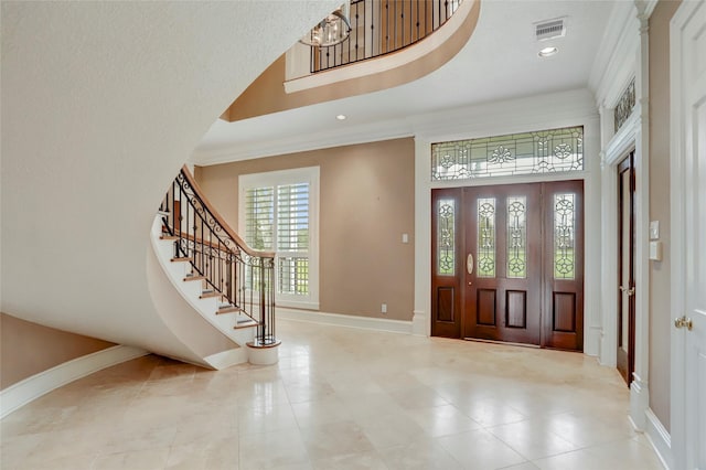 foyer entrance with visible vents, crown molding, a high ceiling, and baseboards