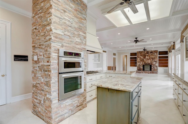 kitchen with a ceiling fan, a stone fireplace, appliances with stainless steel finishes, beamed ceiling, and open floor plan