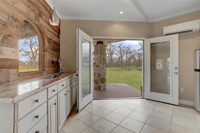 kitchen with crown molding, light stone countertops, a wall unit AC, white cabinets, and a sink