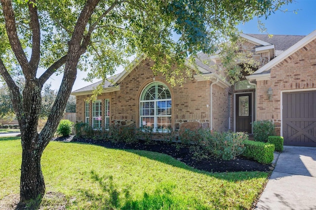 view of front facade with a front yard, an attached garage, brick siding, and driveway