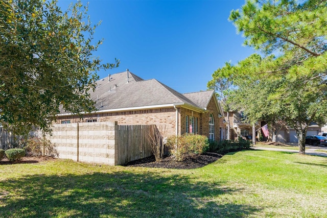 view of property exterior featuring brick siding, fence, a yard, and roof with shingles