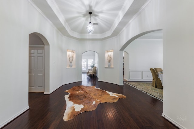 foyer featuring wood finished floors, baseboards, a tray ceiling, arched walkways, and ornamental molding