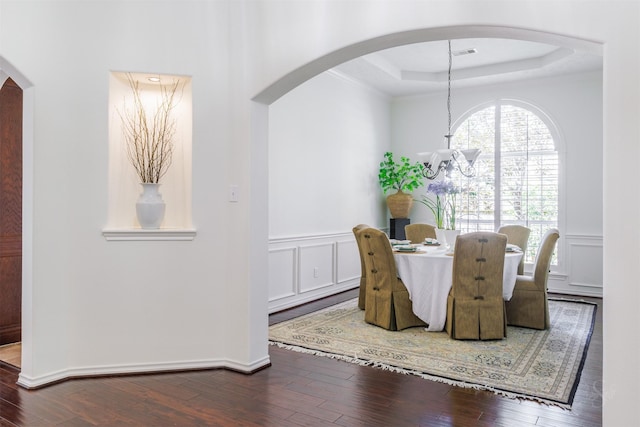 dining space with visible vents, hardwood / wood-style floors, a notable chandelier, a decorative wall, and a raised ceiling