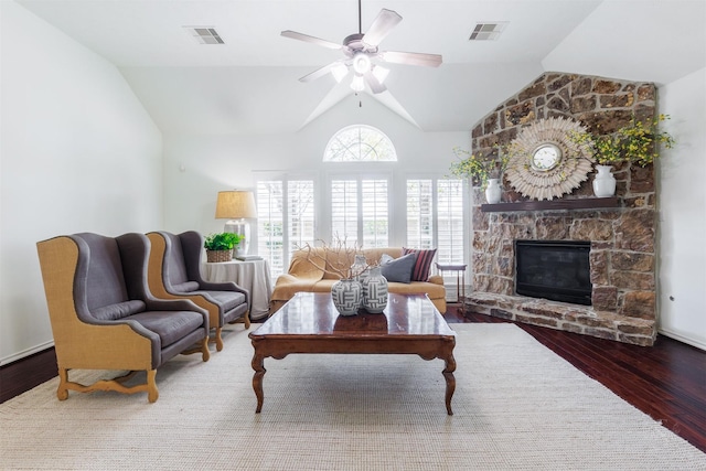 living room featuring a ceiling fan, wood finished floors, visible vents, lofted ceiling, and a stone fireplace