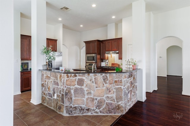 kitchen featuring visible vents, appliances with stainless steel finishes, a high ceiling, arched walkways, and dark wood-style flooring