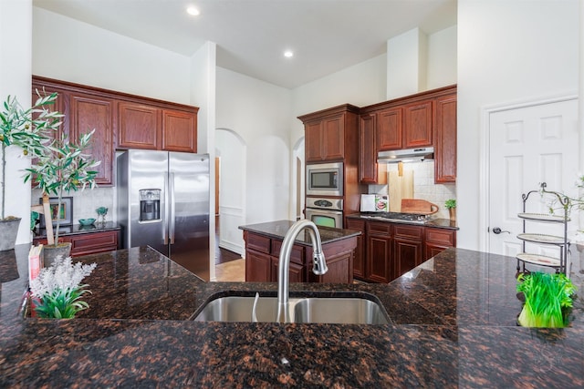 kitchen featuring arched walkways, a sink, under cabinet range hood, appliances with stainless steel finishes, and tasteful backsplash