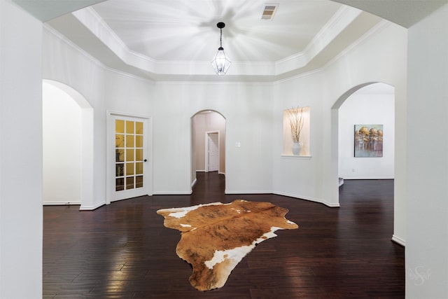 unfurnished room with visible vents, a tray ceiling, arched walkways, wood-type flooring, and crown molding