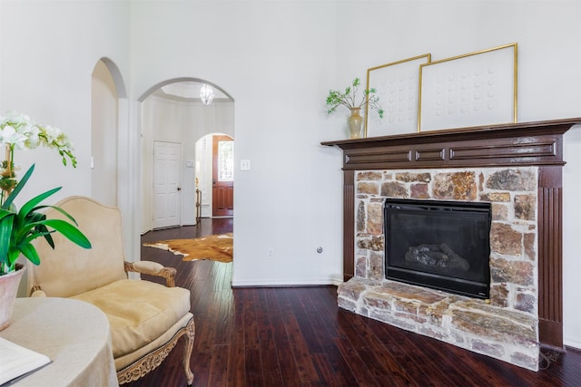 living room featuring arched walkways, a stone fireplace, baseboards, and wood-type flooring