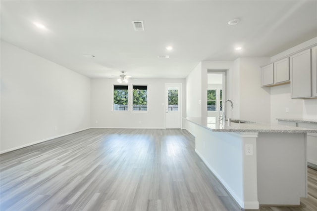 kitchen featuring light stone countertops, a center island with sink, visible vents, light wood finished floors, and a sink