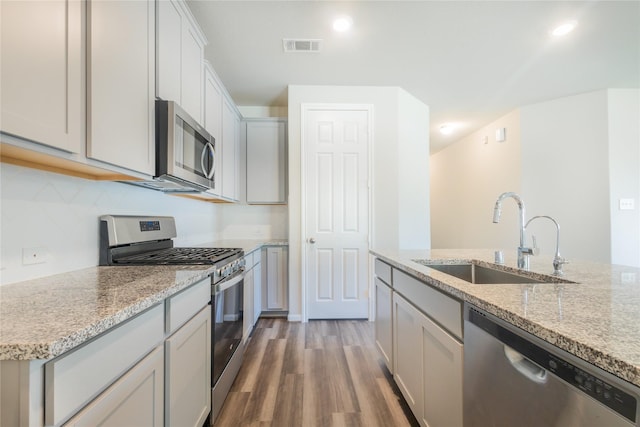 kitchen with visible vents, a sink, light stone counters, wood finished floors, and stainless steel appliances