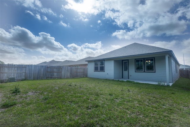 rear view of house featuring a yard, a fenced backyard, and roof with shingles