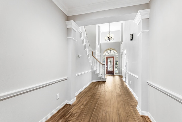 corridor with a notable chandelier, ornamental molding, wood finished floors, stairway, and baseboards