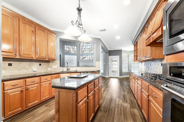 kitchen with visible vents, a kitchen island, dark stone counters, appliances with stainless steel finishes, and a sink