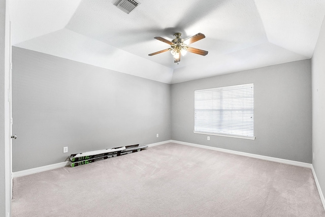 carpeted empty room featuring visible vents, baseboards, ceiling fan, vaulted ceiling, and a raised ceiling