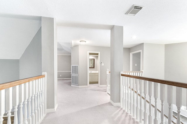 hallway featuring an upstairs landing, visible vents, baseboards, and carpet