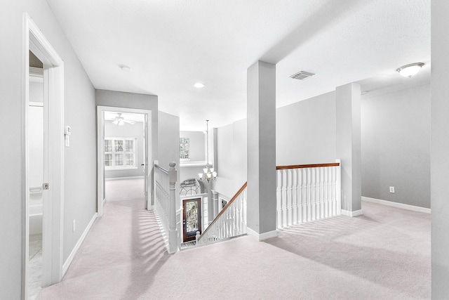 corridor featuring visible vents, baseboards, an inviting chandelier, carpet flooring, and an upstairs landing