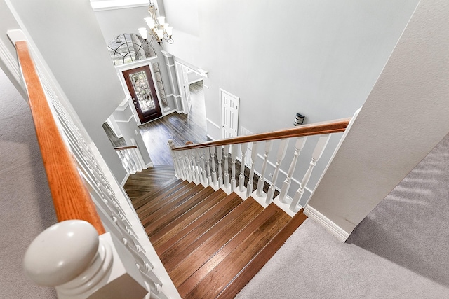 stairs with an inviting chandelier, a high ceiling, wood finished floors, and baseboards