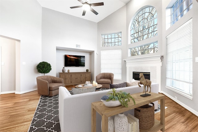 living room featuring baseboards, a ceiling fan, wood finished floors, and a high end fireplace