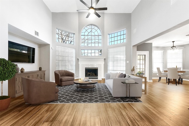 living area with visible vents, wood finished floors, a high ceiling, a fireplace, and ceiling fan