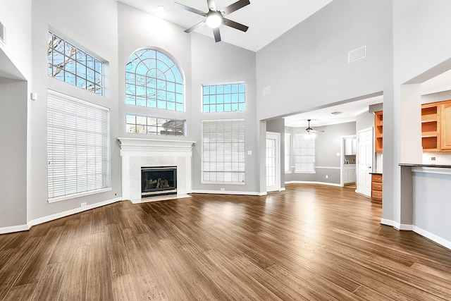 unfurnished living room with a ceiling fan, a high ceiling, a premium fireplace, baseboards, and dark wood-style flooring