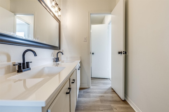 bathroom with a sink, baseboards, wood finished floors, and double vanity