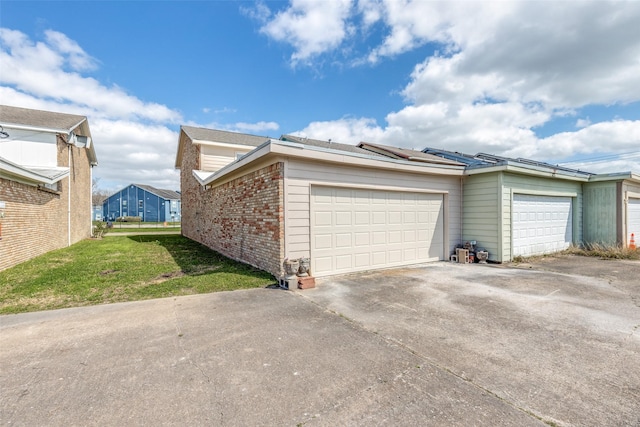 view of home's exterior with a yard, an attached garage, concrete driveway, brick siding, and roof mounted solar panels