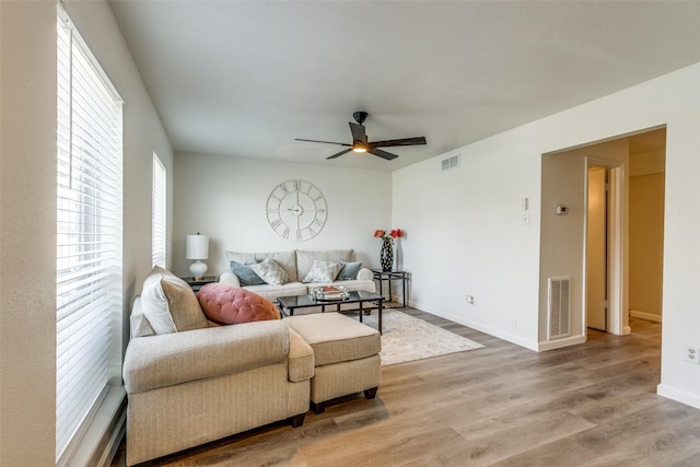 living area featuring visible vents, baseboards, light wood-style floors, and a ceiling fan